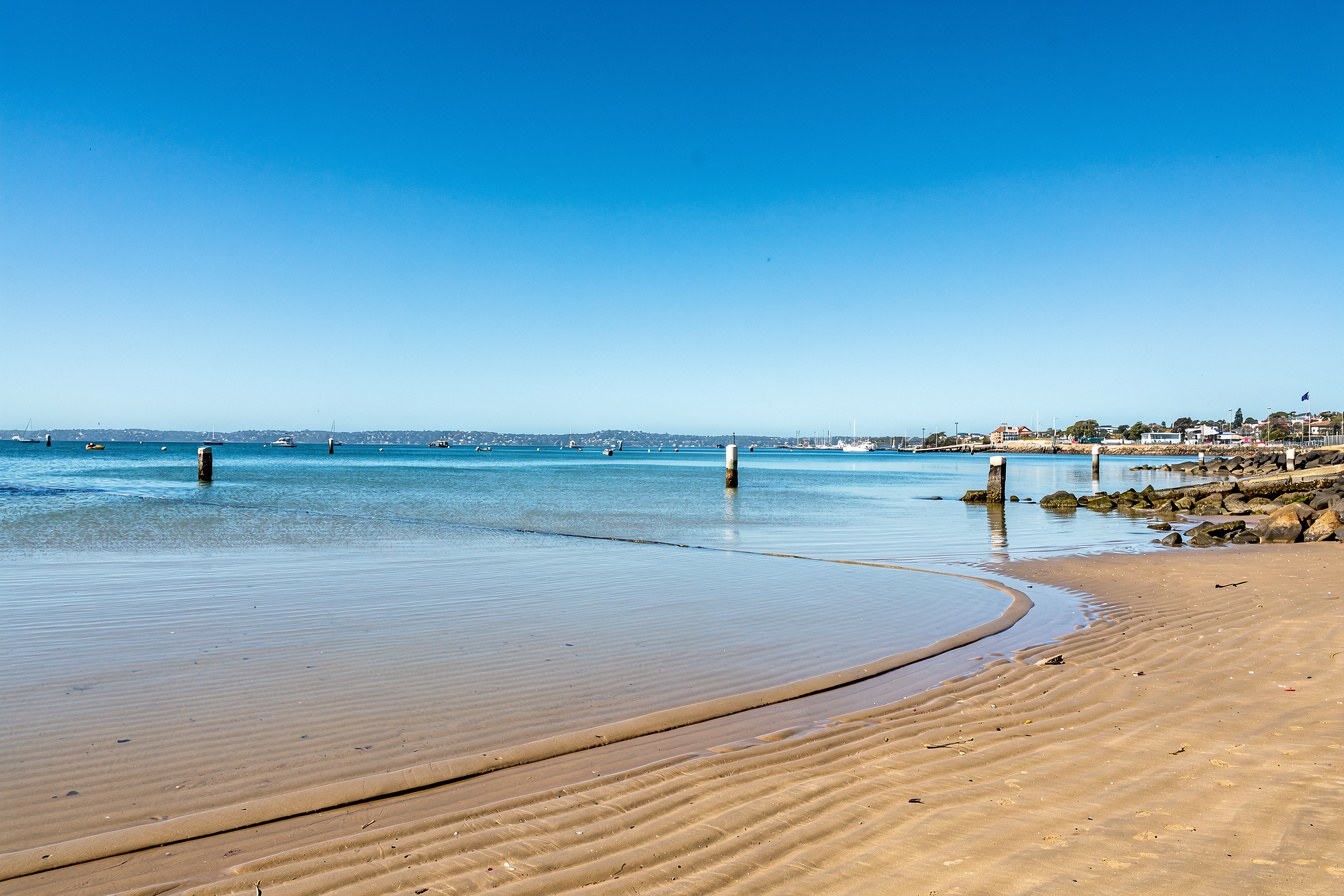 An empty tide line on wet sand at a harbour, marking where the water has been and where it may return.